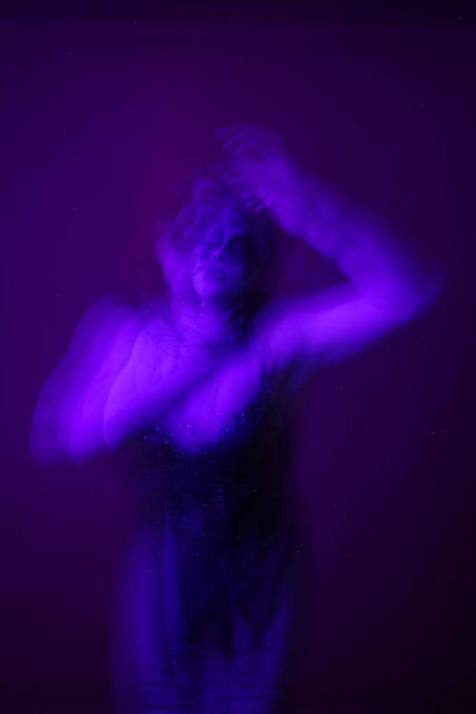 A blurred abstract portrait of a person in motion with vibrant purple lighting, evoking mystery.