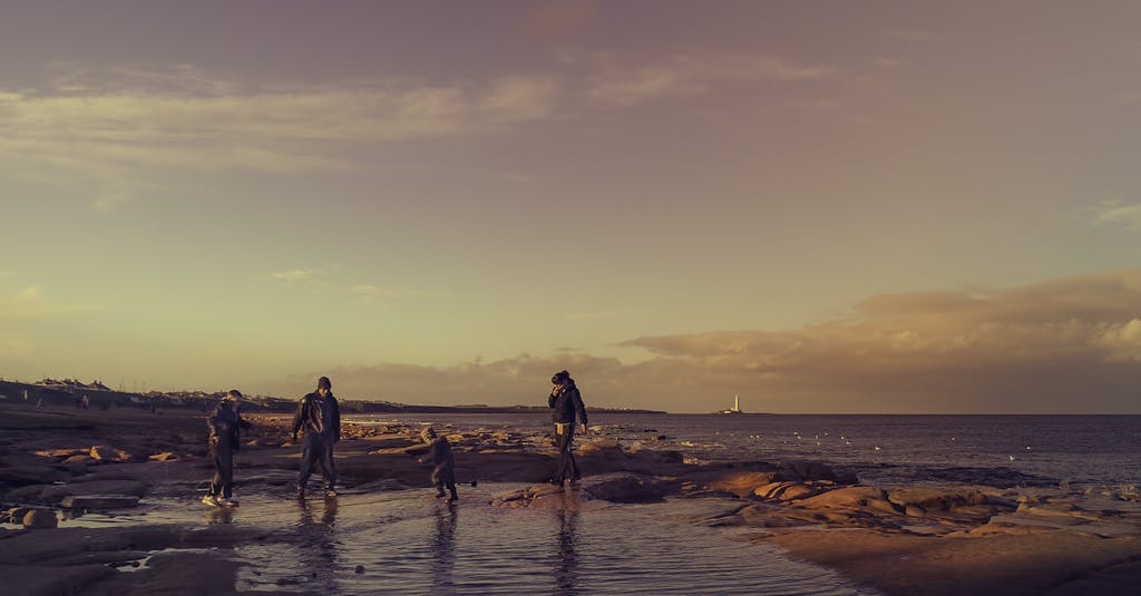 A family of four walking on a beach during a beautiful sunset near a lighthouse.