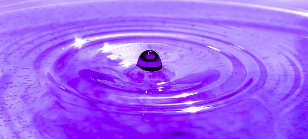 Captivating macro of a droplet creating ripples on a purple liquid surface.